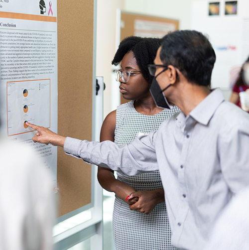 Two student interns looking and pointing at a poster presentation.