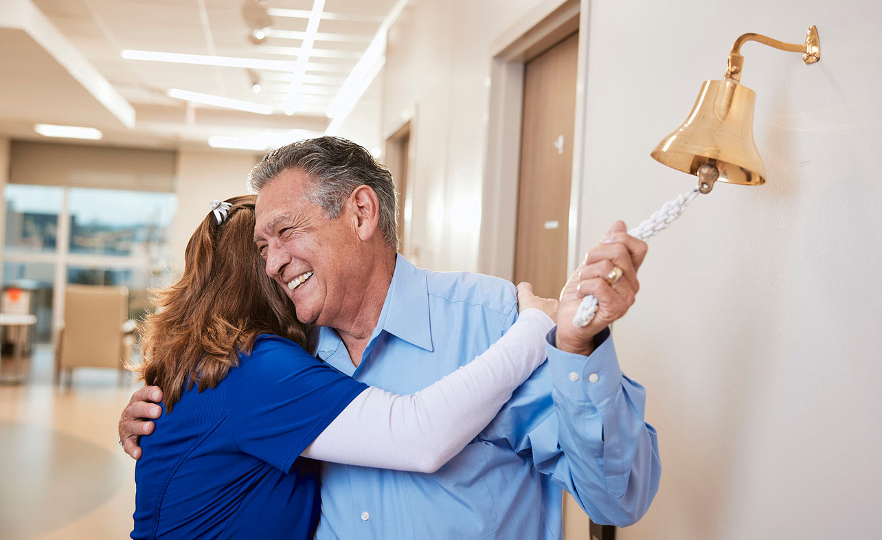 A nurse hugs a patient as he rings the bell celebrating the completion of cancer treatment