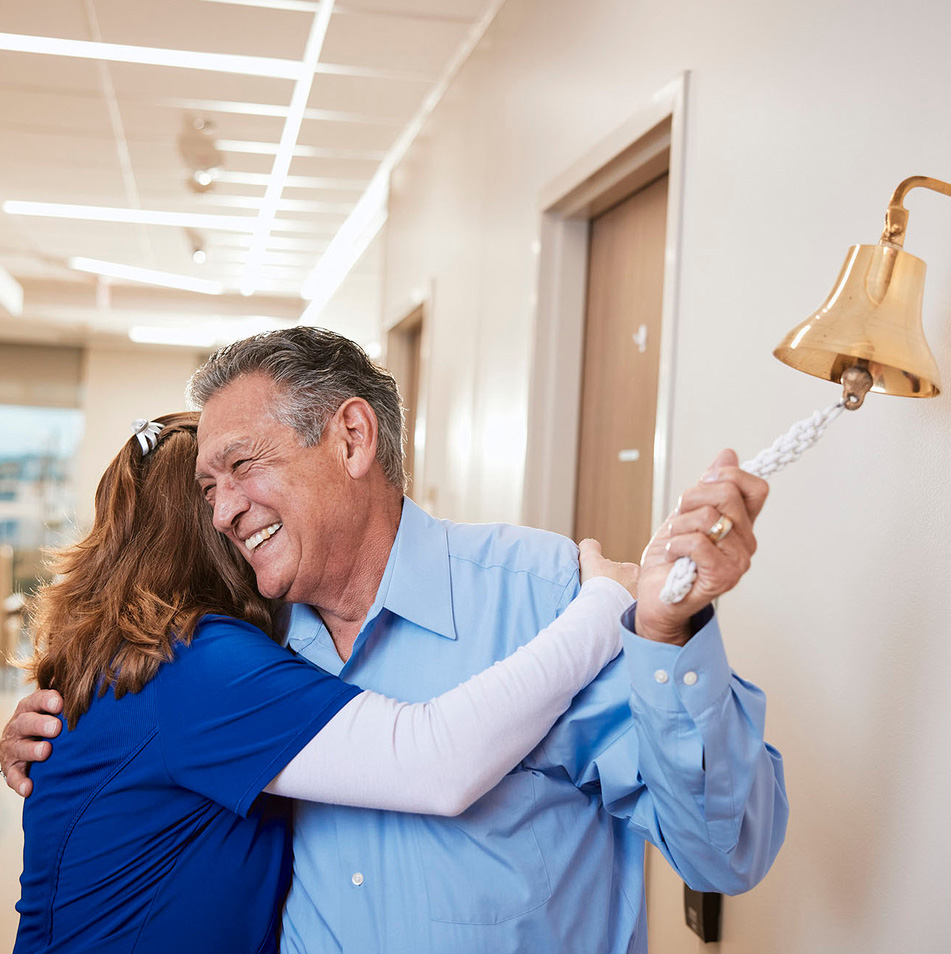 A nurse hugs a patient as he rings the bell celebrating the completion of cancer treatment