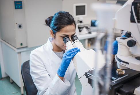 Female researcher in a lab coat examines samples under a microscope