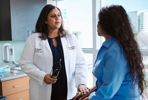 Sukeshi Patel Arora, MD, speaks with a woman in blue shirt in a clinical space.