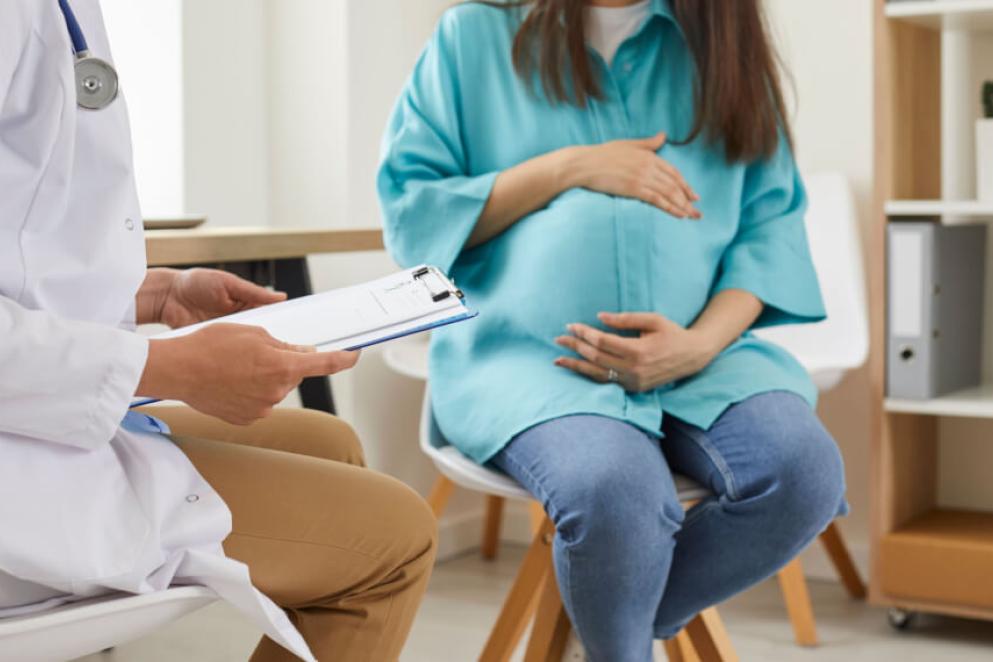 pregnant woman sitting at the desk in doctor's office visiting clinic. Health provider holding report file and giving consultation during medical exam